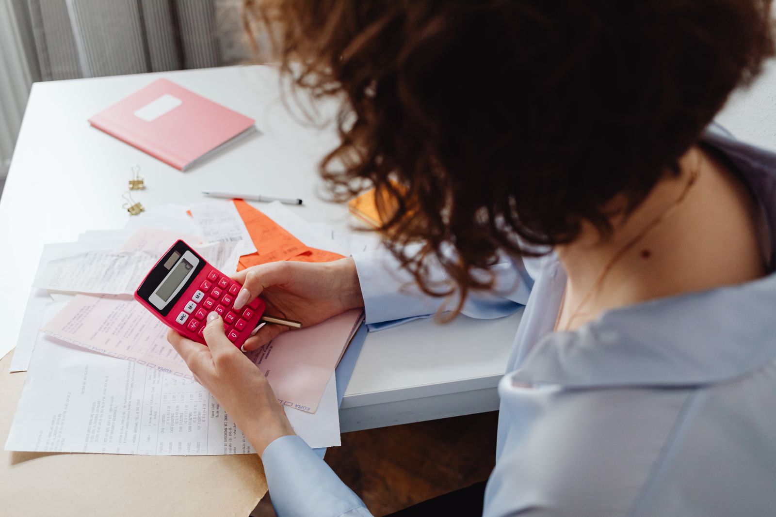 A woman calculating expenses with documents and a calculator at a work desk